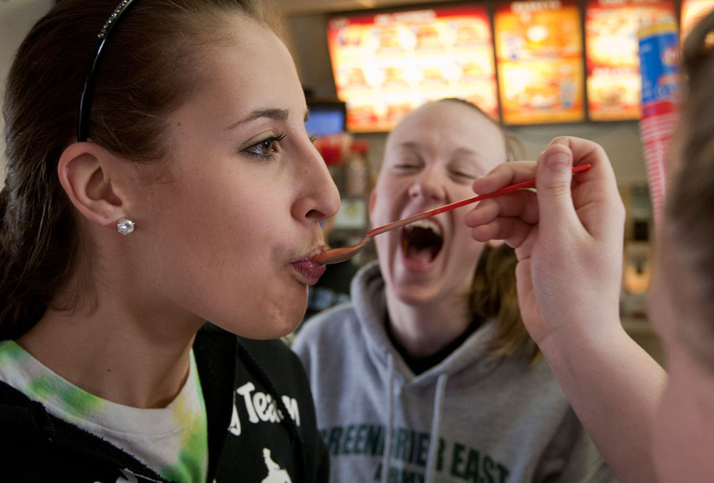 After convincing their coaches to stop at Dairy Queen, Senior Kayla Whited eats a bite of a Blizzard served to her by sophomore Maddee Carroll while senior Katie Abell watches following an elementary school visit Tuesday afternoon.