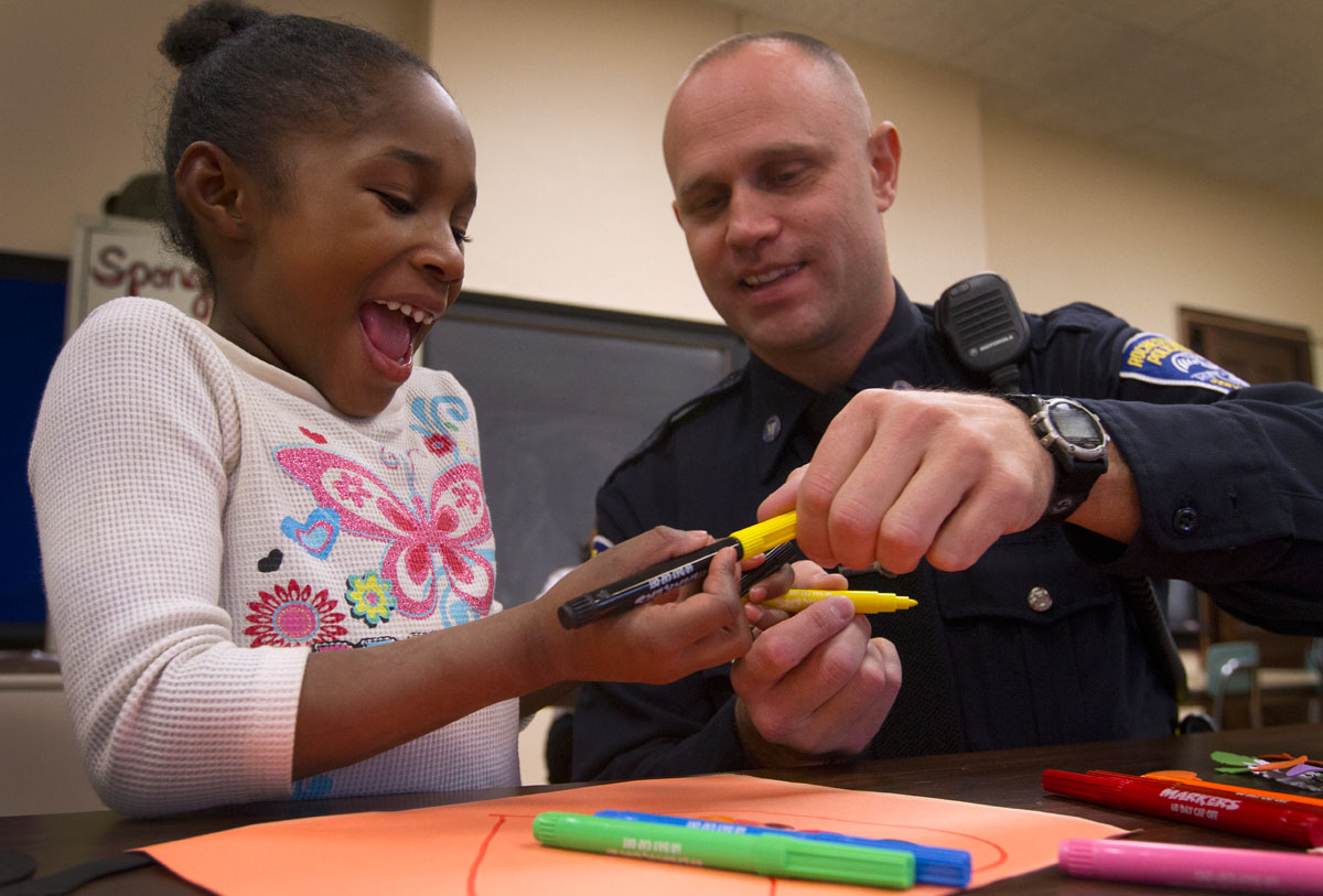 First-grader Jayla Simms laughs while Rochester police officer Jim Perry jokes about putting mismatching caps on her markers Oct. 31 at School 36, Henry W. Longfellow School. Perry, who patrols on the west side of Rochester, spends time with first graders once a week as part of Generation Two mentoring. This is Perry's second year volunteering with the program.